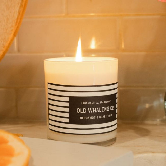 Side view of a Bergamot & Grapefruit candle with a lit, glowing wick