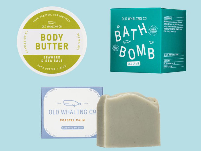 Collection of coastal Old Whaling Co. skincare products including body butter, bath bomb, and soap on a light blue background.