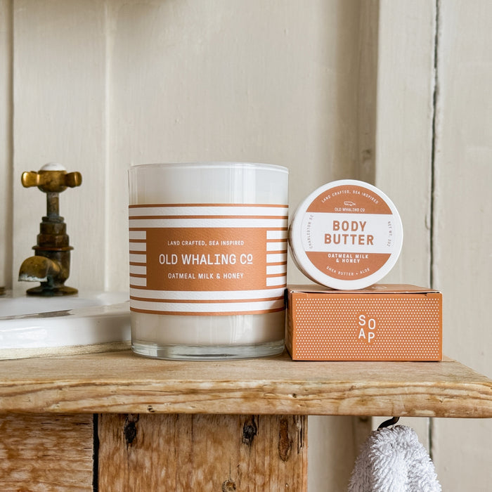 Close up of Oatmeal Milk & Honey Candle, Travel Size Body Butter, Bar Soap on wood sink