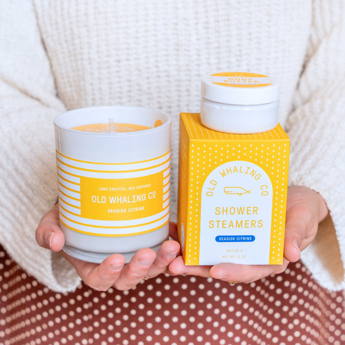 Hands holding Seaside Citrine Candle, Shower Steamers, and Travel Size Body Butter